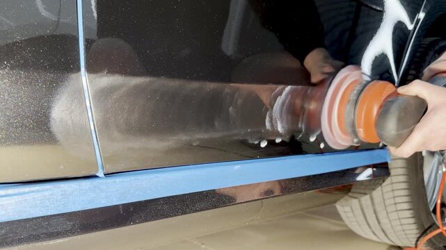 A car service worker polishes the car body with a polishing machine. Detailing and polishing of the car. Car detailing - hands with an orbital polishing machine in an auto repair shop. 