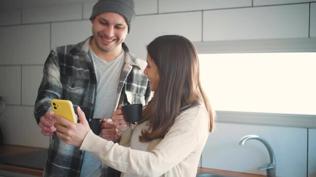 4K video of a young Hispanic couple drinking coffee while laughing and watching social media reels on their mobile phone. Concept of everyday lifestyle, emotional wellbeing, and a healthy romantic rel