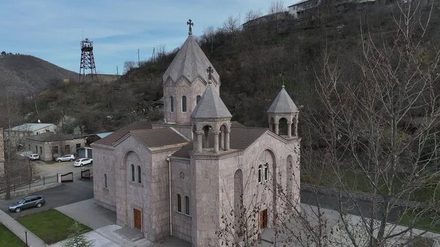 Aerial view of Saint Gregory of Narek Church in Kapan, showcasing its beautiful traditional tuff stone architecture, distinct domes, and scenic mountain landscape in the surrounding background