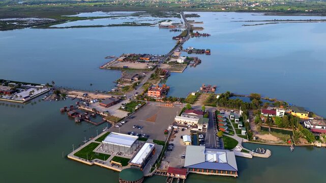 Aerial video featuring  waterfront hotels, restaurants, parking lots, and wooden fishing cabins along the Patok Lagoon in Albania.