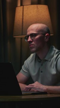 Man in glasses stock trader in home office. Male analyzes terminal, trades stocks on crypto market. Smartphone monitor and laptop display vivid candlestick chart, trading charts, price action. Evening