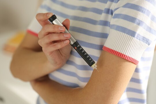Diabetes. Woman making insulin injection into her arm with autoinjector indoors, closeup