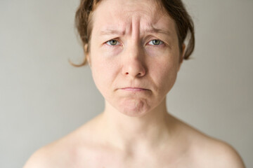 Fototapeta premium Woman Frowning Furrowed Brow Looking Directly At Camera With Bare Shoulders Neutral Background Soft Lighting Conveying Concern Or Dissatisfaction.