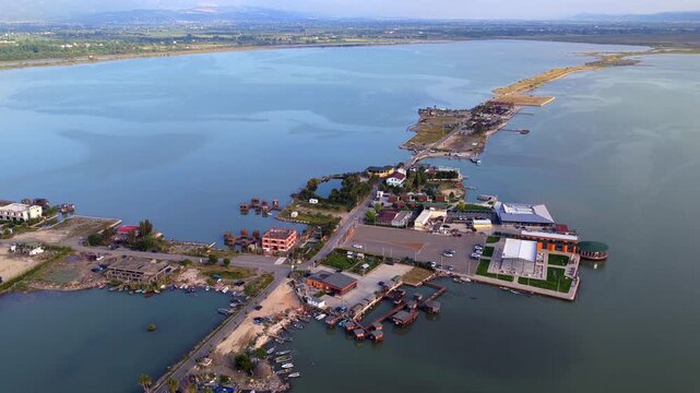 Aerial video featuring a slender land spit packed with seafood restaurants, stilt cabins, and open parking lots in Patok, Albania.