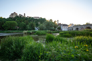 Fototapeta premium Historic castle on a hill overlooking a river with ducks, stone bridge and traditional houses. Harburg, Bavaria, Germany.