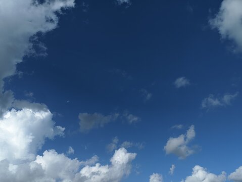 Blue sky background with white cumulus clouds creating a natural frame. Offers ample copy space perfect for background, wallpaper, graphic design, presentation backdrop.