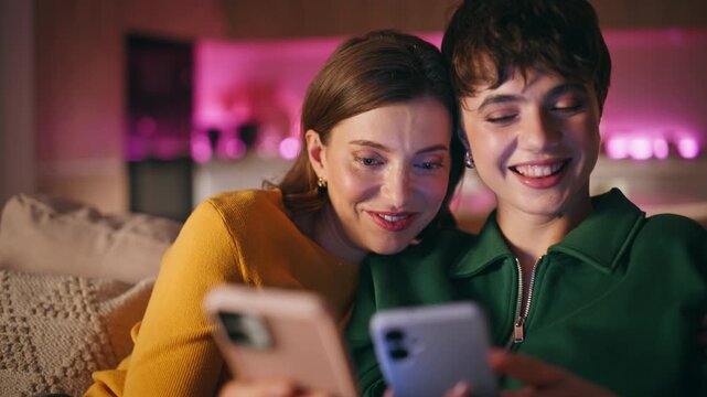 Cheerful besties looking mobile phone chatting in social media browsing content.