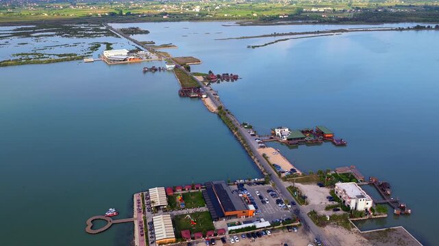 Aerial video featuring a slender land spit packed with seafood restaurants, stilt cabins, and open parking lots in Patok lagoon, Albania.