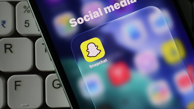 Closeup of a smartphone screen showing the snapchat app icon inside a social media folder, with a computer keyboard visible in the background