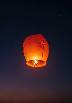 Floating glowing paper lantern released at night, ascending high into the dark atmospheric heavens during a spiritual ceremony, hot air, evening, twilight