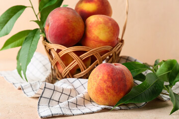 Obraz premium Wicker basket with sweet ripe peaches and leaves on beige background