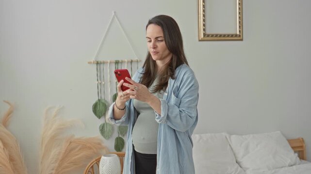 Woman holding red smartphone with outstretched hand, smiling by bed with rattan chair, pampas grass and macrame wall hanging in bedroom; serenity connection.