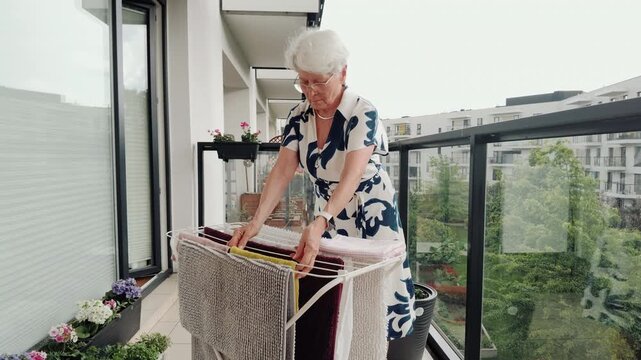 Senior Woman Hanging Laundry on Balcony 