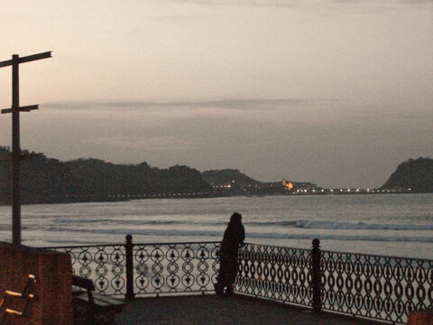 Persona apoyado en una barandilla mirando el mar al atardecer