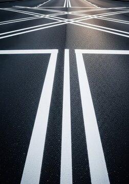 A high-contrast view of wide white parallel lines painted across the dark gray asphalt surface of a roadway intersection for safety purposes, traffic, black, stripe