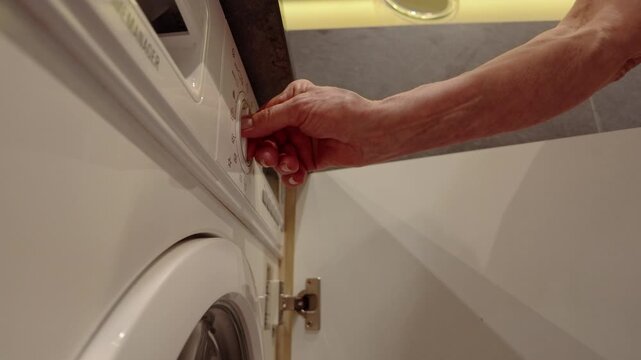 Senior Woman Turning On Washing Machine
