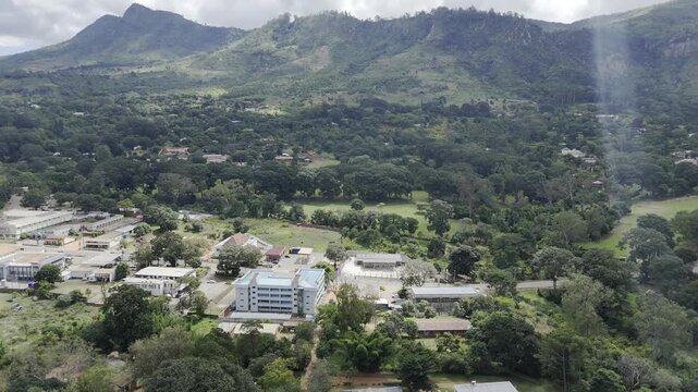 Drone orbits right along main road next to golf course at base of mountain on a sunny day in Zomba, Malawi