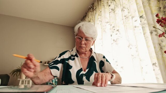 Senior Woman Checking Household Bills and Documents at Table  