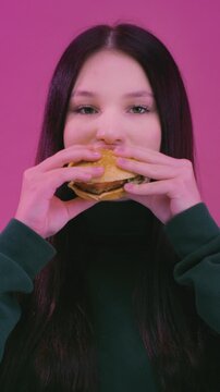 Caucasian teen woman girl eating junk fast food, bite burger hamburger cheeseburger, eat unhealthy meal, diet nutrition disorder, cheat meal overeating calories. Teenager biting patty