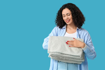 Beautiful young African-American woman with cozy folded blanket on blue background © Pixel-Shot