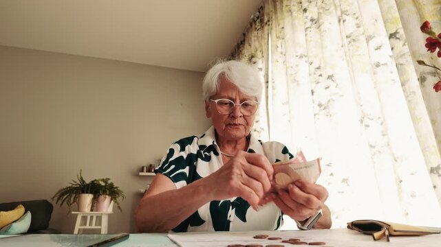 Senior Woman Counting Euro Banknotes and Coins at Table 