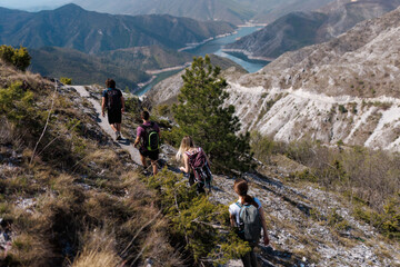 Fototapeta premium Group of hikers exploring mountain trail near lake in daytime under clear sky
