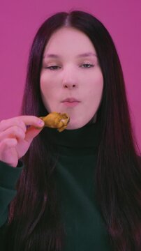 Teen girl eating fried chicken meat wings. Unhealthy fast street food snack, crispy junk. Protein lunch, high calories. Young woman biting nuggets. Youth culture and indulgence concept.