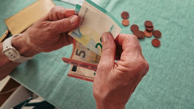 Senior Woman Counting Euro Banknotes and Coins at Table 