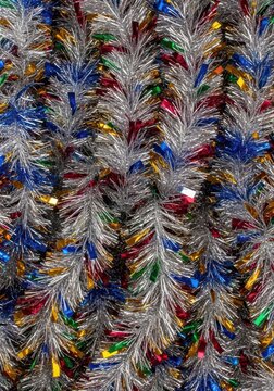 A shimmering, vibrant background texture created entirely by densely packed metallic strands of silver and colorful tinsel decorations, shiny, macro, silver