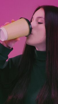 Teen brunette girl enjoying hot tea. Young woman holding take away coffee paper cup, cardboard. Female drink warm beverage, casual lifestyle moment, cozy mood. Student takes a sip from a paper cup