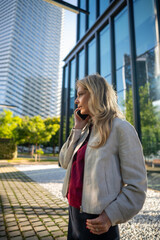 Fototapeta premium Businesswoman having phone call outside modern office building