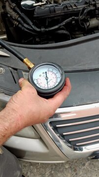 A hand holds a compression gauge over an open engine