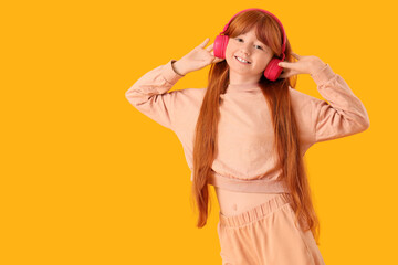 Smiling redhead girl listening to music in pink headphones on bright yellow background with copy...