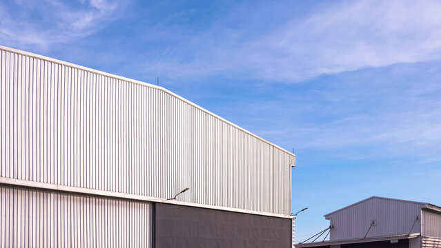 Industrial warehouse buildings with corrugated metal cladding against blue sky. Exterior of commercial factory or storage facility under bright daylight