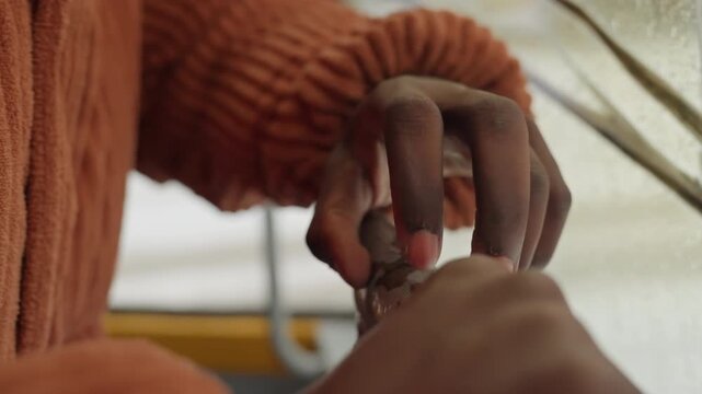 Intimate package unveiling. Woman opening small package carefully. Closeup of fingers revealing tiny wrapped item. Black woman delicately unwrapping miniature package with textured fingertips