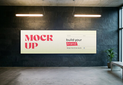 Horizontal panoramic billboard mockup mounted on a black slate tile wall in a modern office lobby or exhibition interior with overhead linear lights and a potted plant