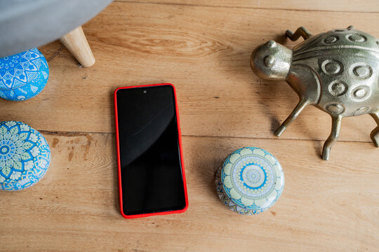 Tel&eacute;fono inteligente con funda roja sobre mesa de madera junto a objetos decorativos modernos