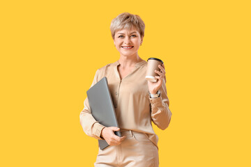 Mature businesswoman with laptop and coffee cup on yellow background