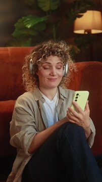Vertical video of curly haired woman browsing dating app and choosing profiles on smartphone at home. High quality 4k footage