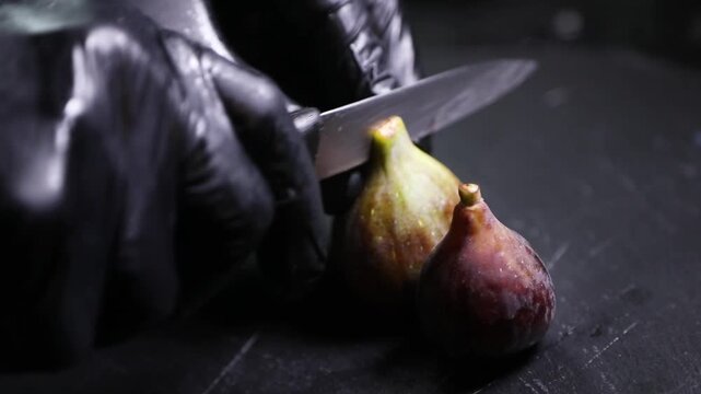 Chef con guantes negros cortando un higo maduro. Chef profesional con guantes negros cortando un higo maduro. Preparaci&oacute;n culinaria artesanal, ingrediente gourmet de temporada.
