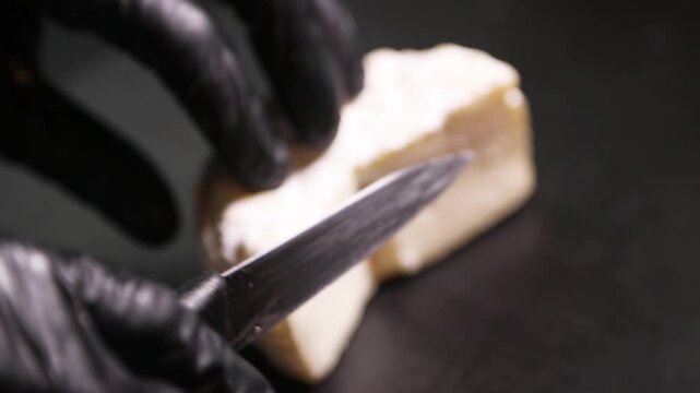 Chef cortando queso de cabra artesanal sobre mostrador negro. Chef profesional rebanando queso de cabra hecho a mano sobre una superficie negra. Productos l&aacute;cteos artesanales, preparaci&oacute;n culinaria 