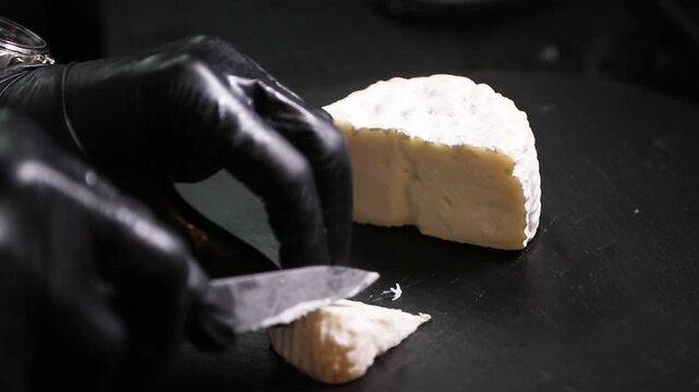Chef cortando queso de cabra artesanal sobre mostrador negro. Chef profesional rebanando queso de cabra hecho a mano sobre una superficie negra. Productos l&aacute;cteos artesanales, preparaci&oacute;n culinaria 