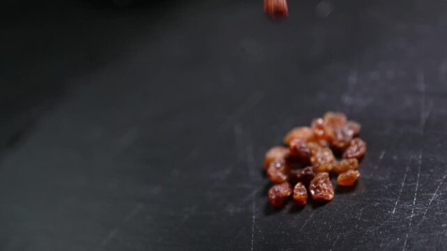 Manos lanzando un pu&ntilde;ado de pasas sobre una encimera negra. Pasas frescas esparcidas sobre una superficie negra. Preparaci&oacute;n de ingredientes culinarios artesanales, proceso de receta gourmet.