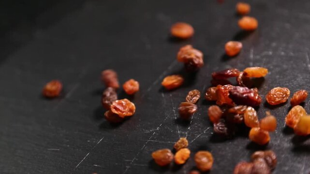 Manos lanzando un pu&ntilde;ado de pasas sobre una encimera negra. Pasas frescas esparcidas sobre una superficie negra. Preparaci&oacute;n de ingredientes culinarios artesanales, proceso de receta gourmet.