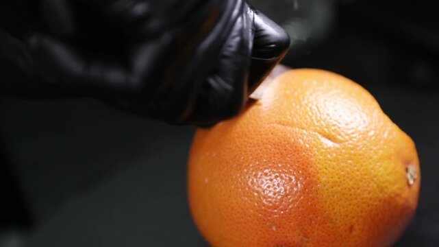 Chef cortando una naranja fresca con un cuchillo sobre una encimera negra. Chef profesional cortando una naranja fresca con un cuchillo. Preparaci&oacute;n culinaria artesanal, ingrediente c&iacute;trico gourmet.