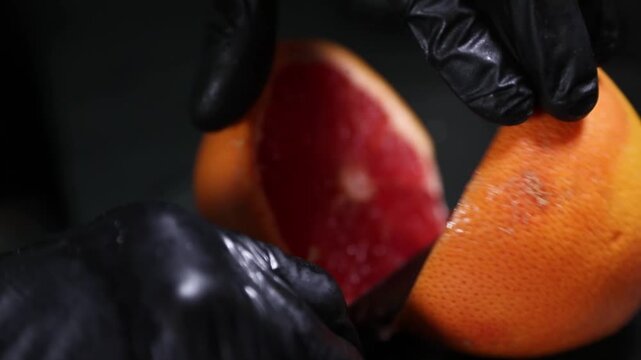 Chef cortando una naranja fresca con un cuchillo sobre una encimera negra. Chef profesional cortando una naranja fresca con un cuchillo. Preparaci&oacute;n culinaria artesanal, ingrediente c&iacute;trico gourmet.