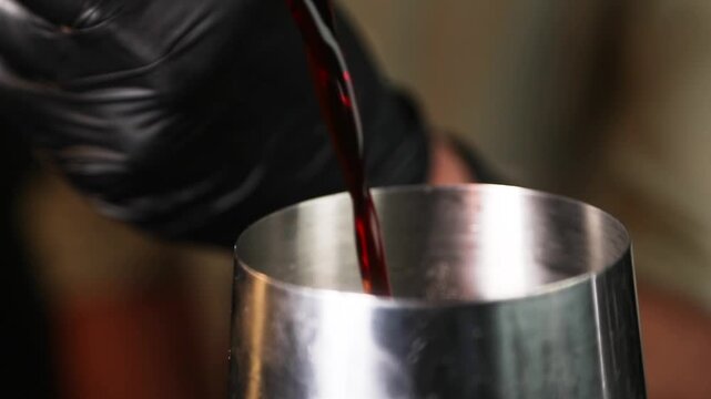 Barman colando l&iacute;quido con colador met&aacute;lico sobre fondo negro. Barman profesional filtrando un c&oacute;ctel con un colador met&aacute;lico. C&oacute;ctel artesanal, t&eacute;cnica de bar precisa, servicio de primera.