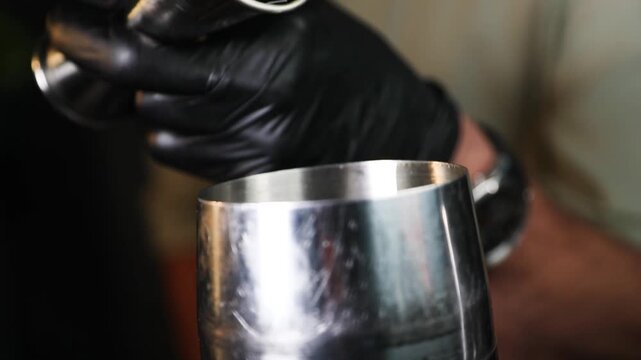 Barman colando l&iacute;quido con colador met&aacute;lico sobre fondo negro. Barman profesional filtrando un c&oacute;ctel con un colador met&aacute;lico. C&oacute;ctel artesanal, t&eacute;cnica de bar precisa, servicio de primera.