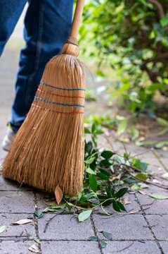 A close up of a classic straw broom in motion sweeping cut branches and leaves on a garden path. Vertical photo.
