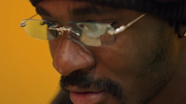 Person in yellow booth reflecting deeply. Thoughtful individual examining screen in quiet setting. Man wearing beanie intensely focusing on his computer screen expressing concentration